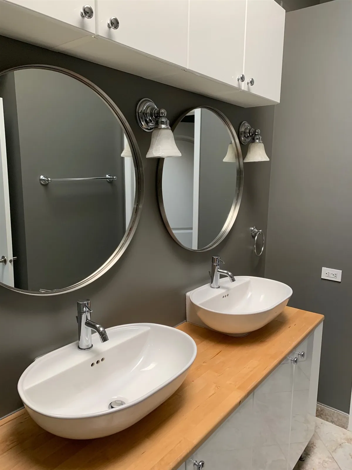 Bathroom with two vessel sinks, round mirrors and dark gray walls