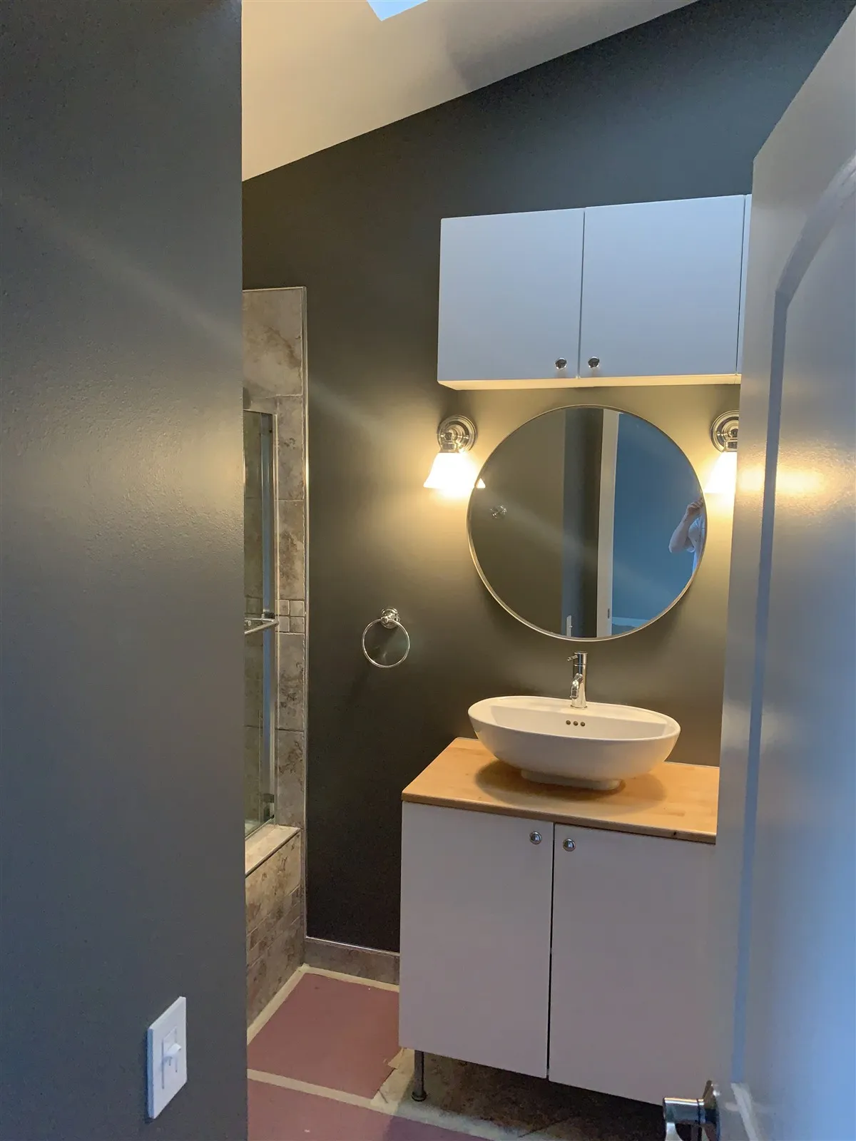 Bathroom with round mirror, vessel sink and wall sconce