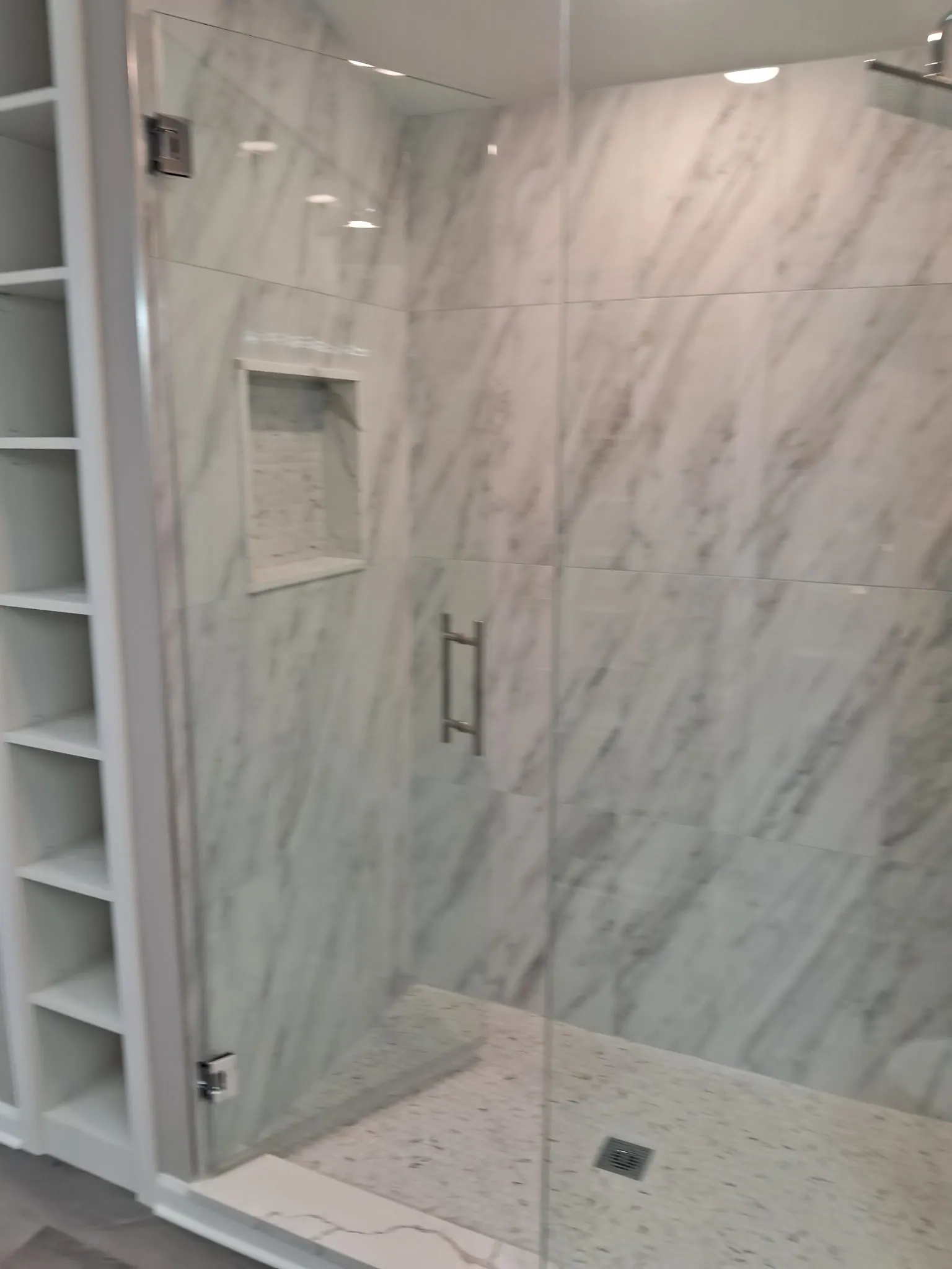 Shower with a built-in niche, marble-look tile and a glass door with a bar handle