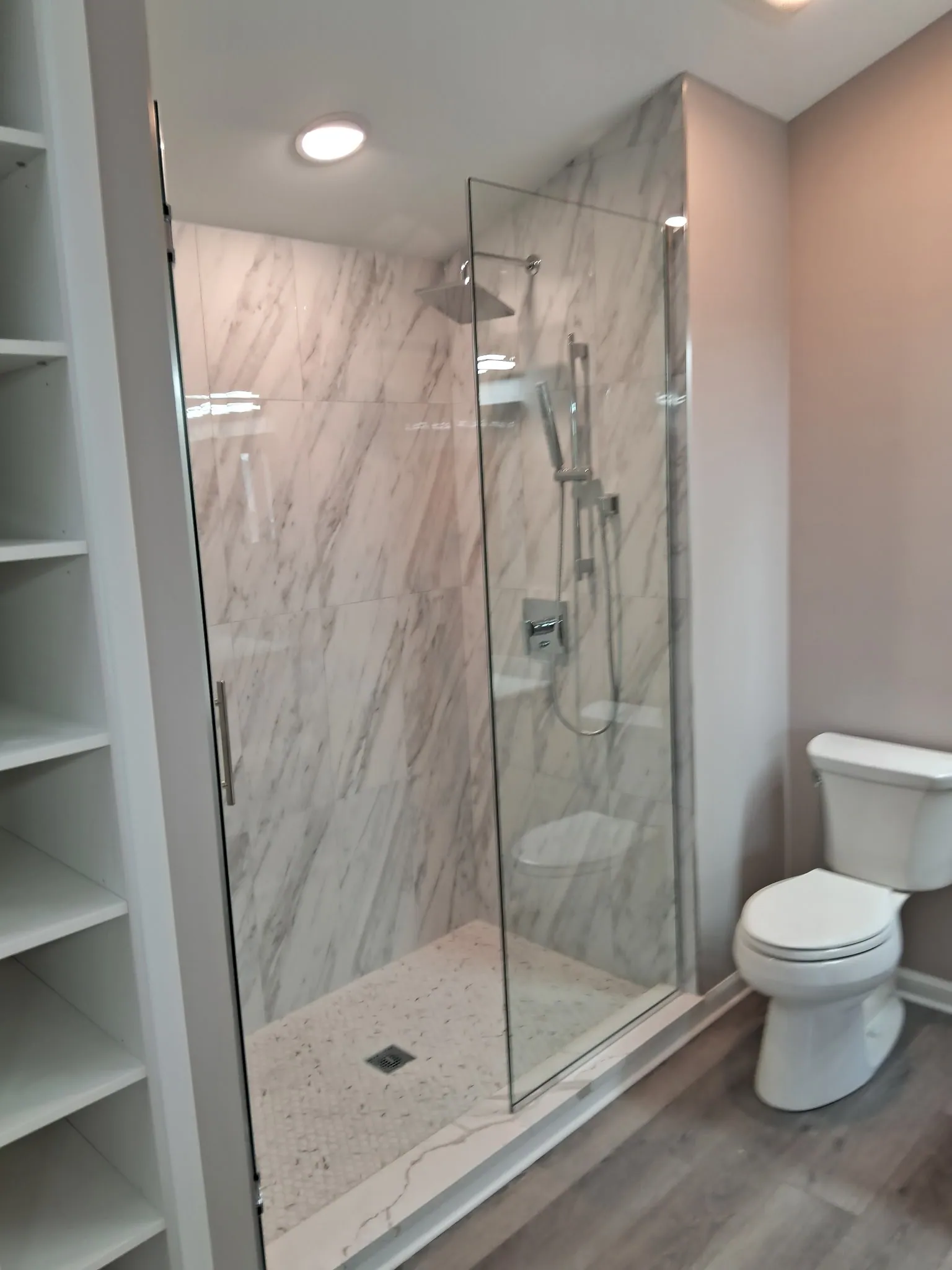 Frameless glass shower with marble-look tile walls and a rain shower head in a remodeled condo bathroom