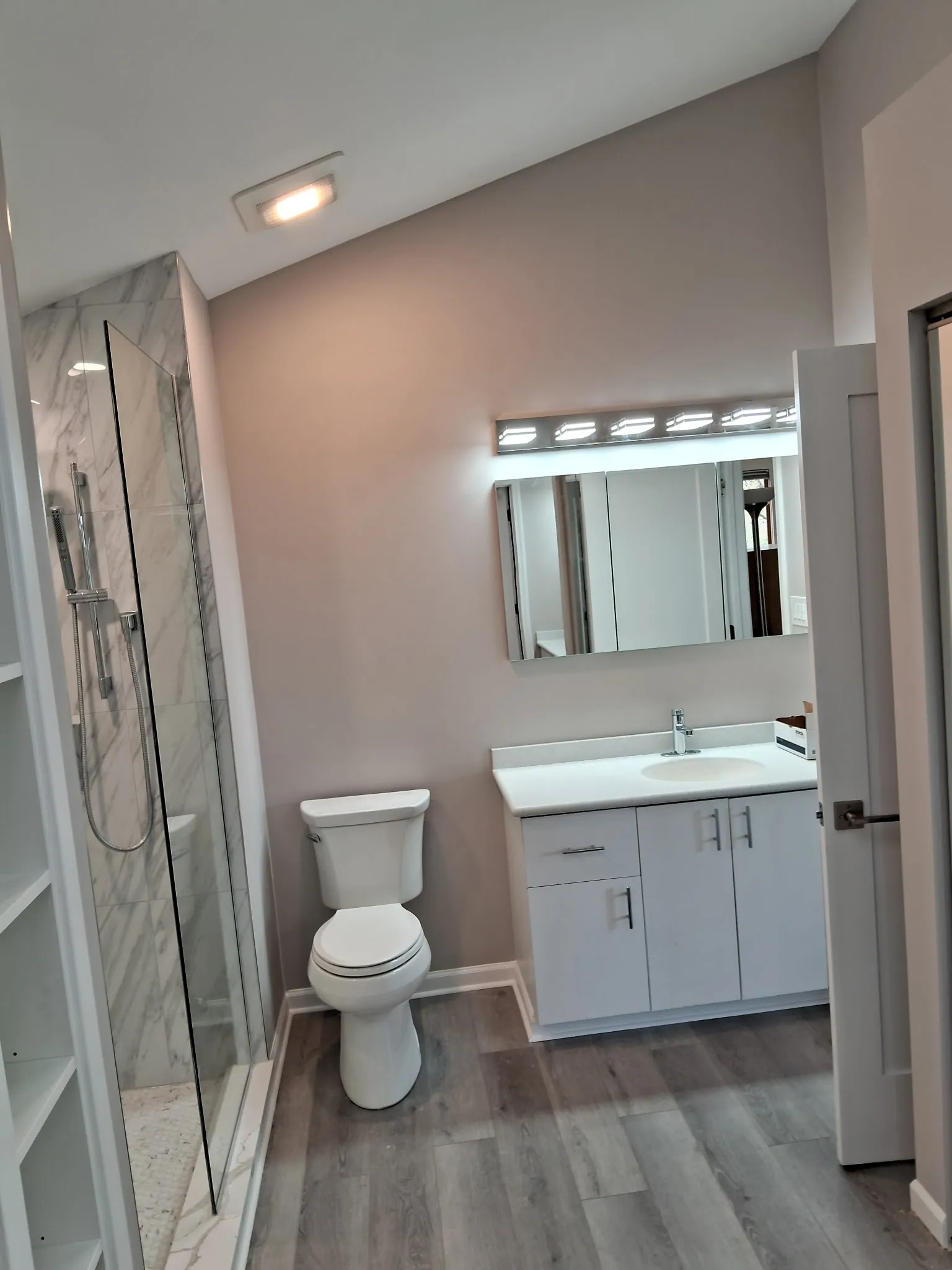 Remodeled condo bathroom with a white vanity, vanity light, toilet and a marble-look glass shower