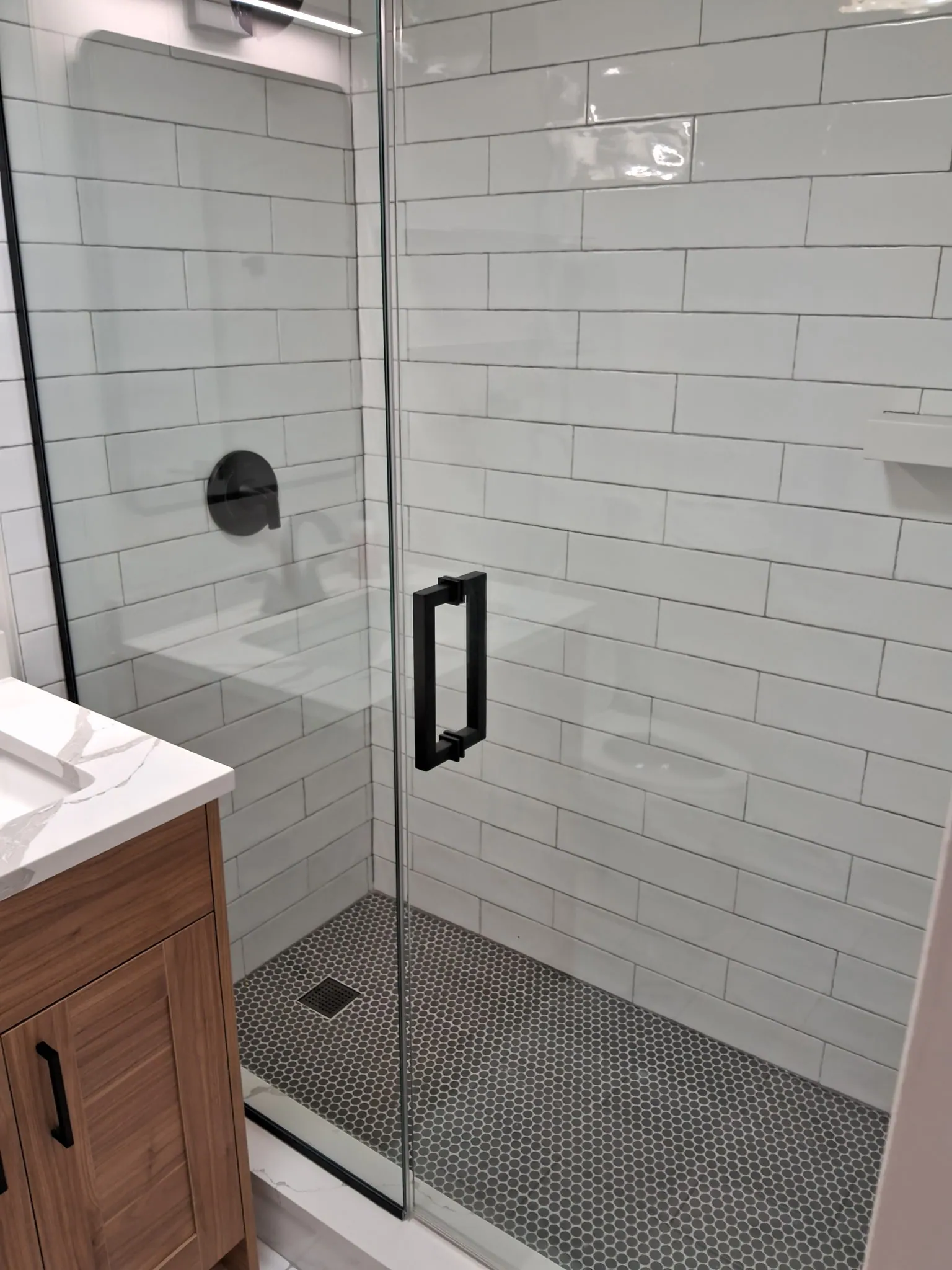 Glass shower enclosure with white subway tile walls, black hardware and a penny tile floor