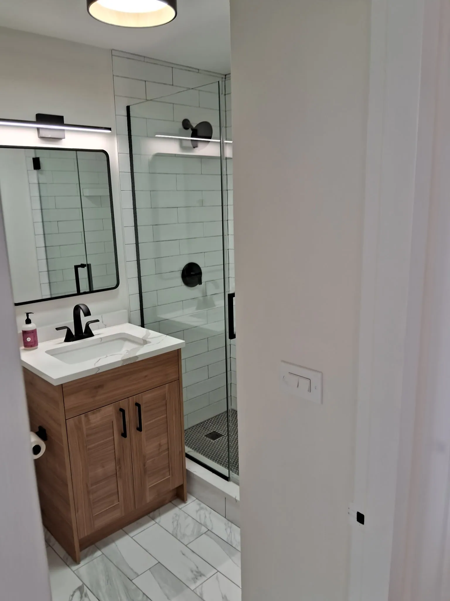 Bathroom vanity with a black faucet and black-framed mirror beside a glass shower enclosure in a Chicago condo remodel