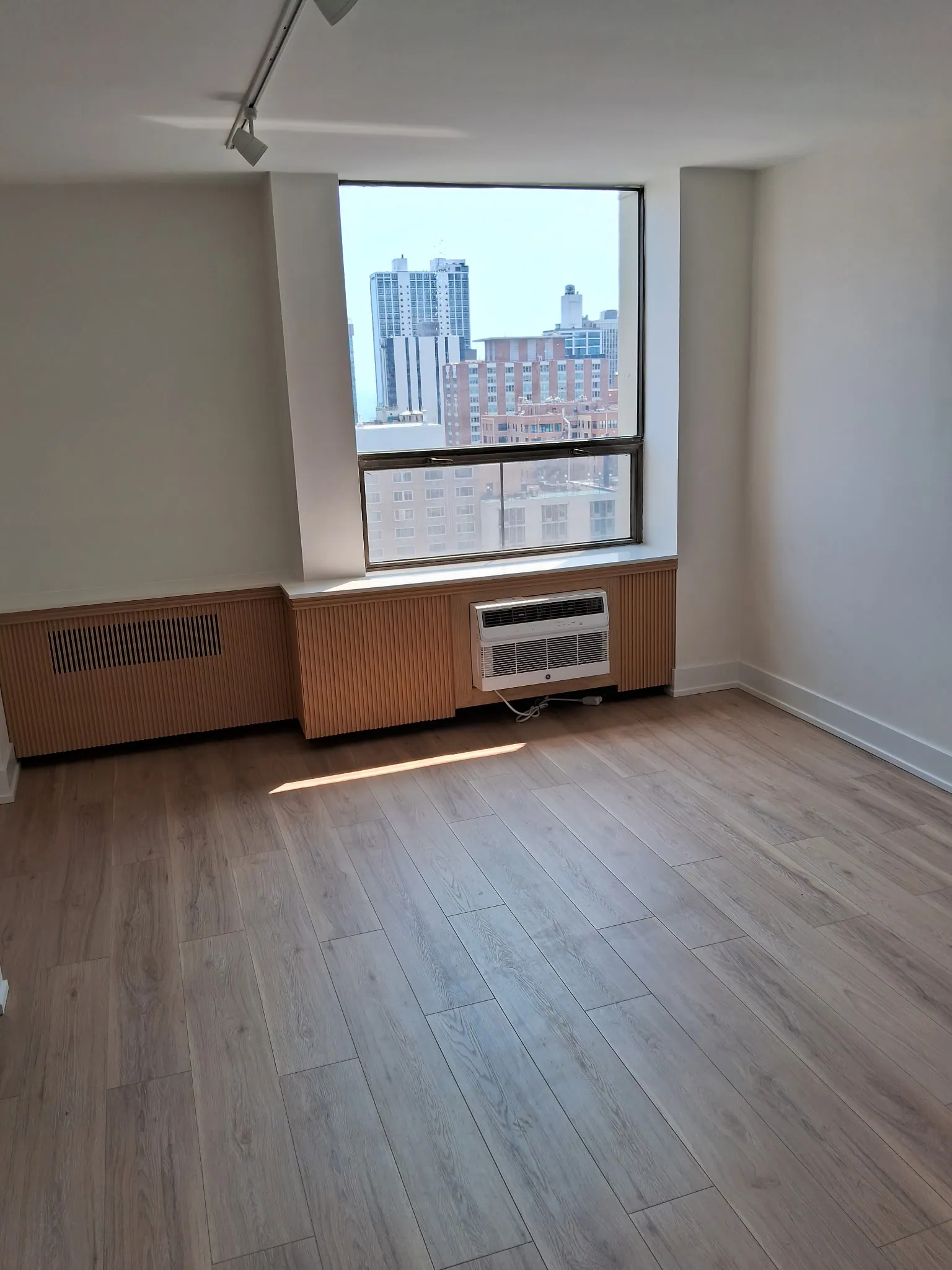 Condo bedroom with new wood-look plank flooring, fresh white trim and a window with a city view