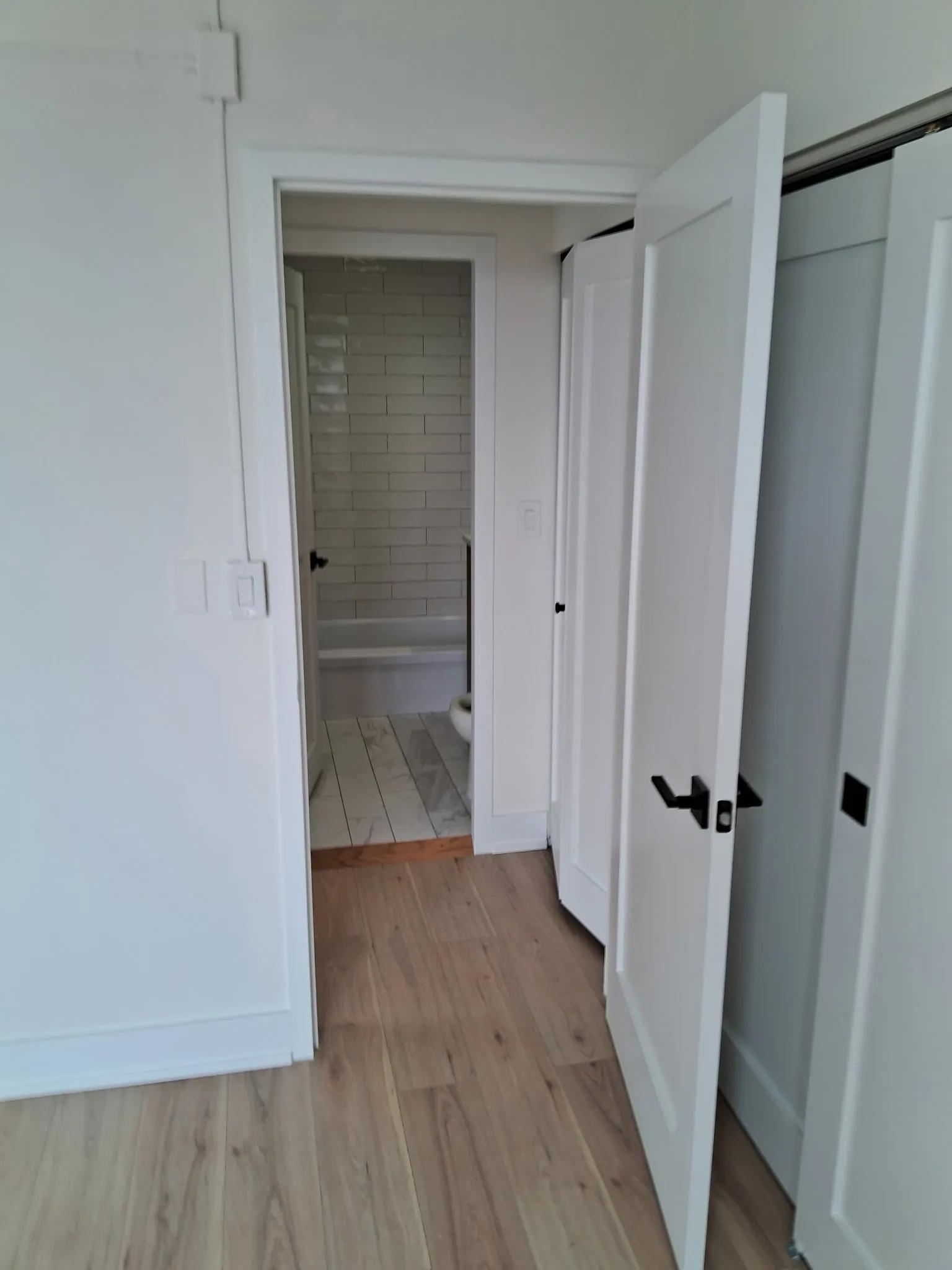 New white interior doors with black handles in a condo hallway, with the remodeled bathroom visible beyond