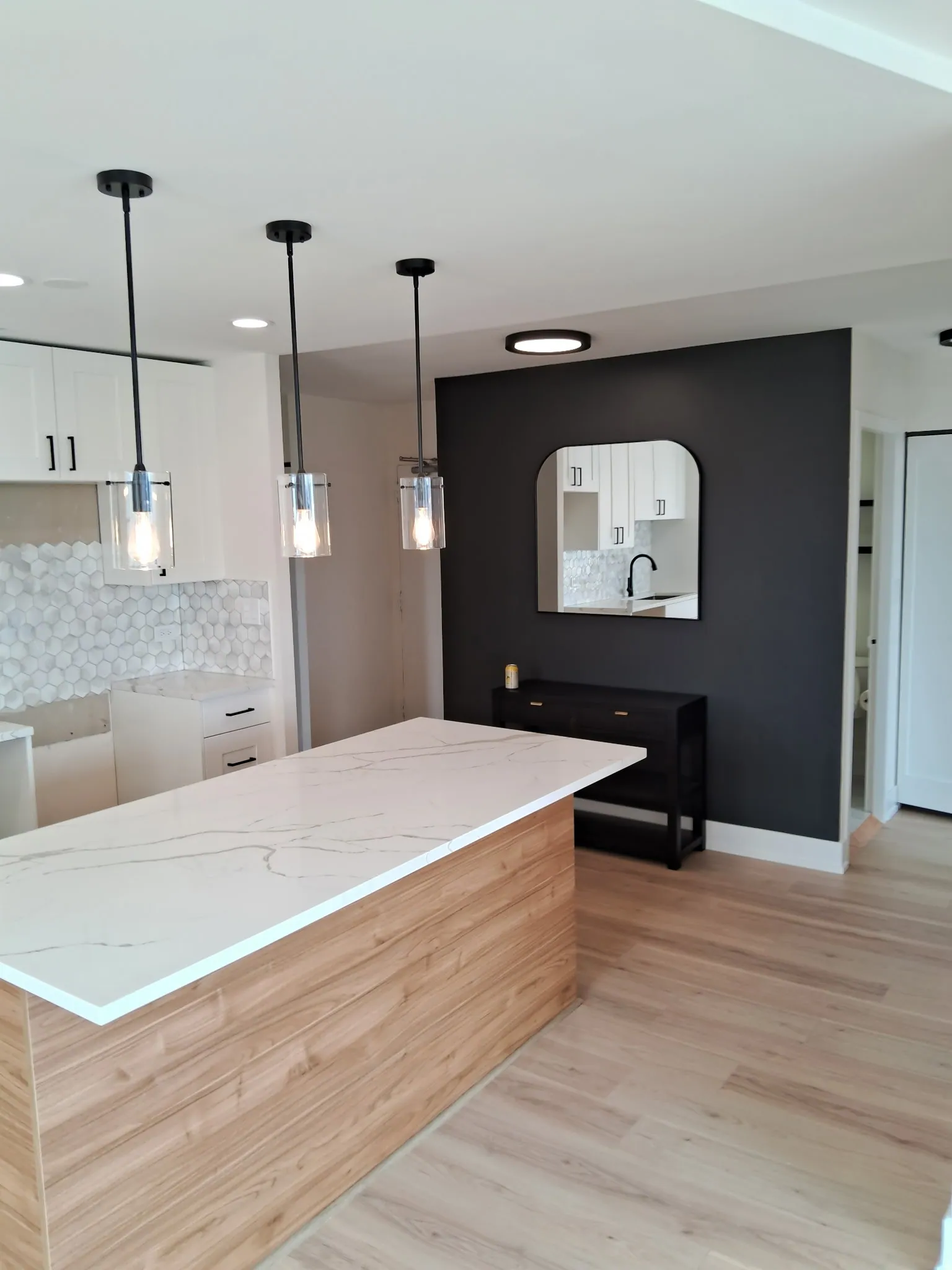 Kitchen island with a white countertop beside a charcoal accent wall and an arched mirror in a remodeled Chicago condo