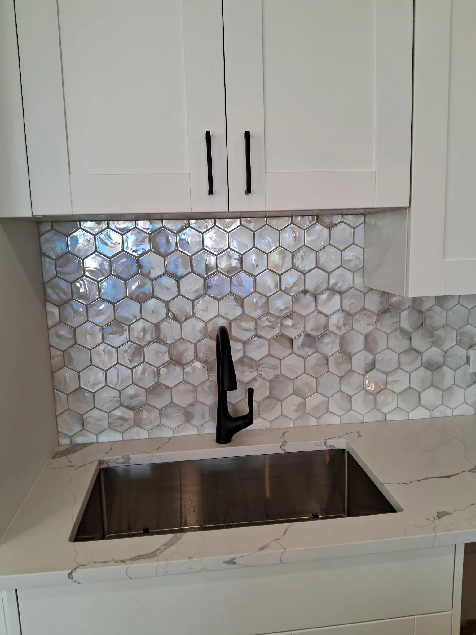 Pearl hexagon tile backsplash, undermount sink and black faucet in a remodeled condo kitchen