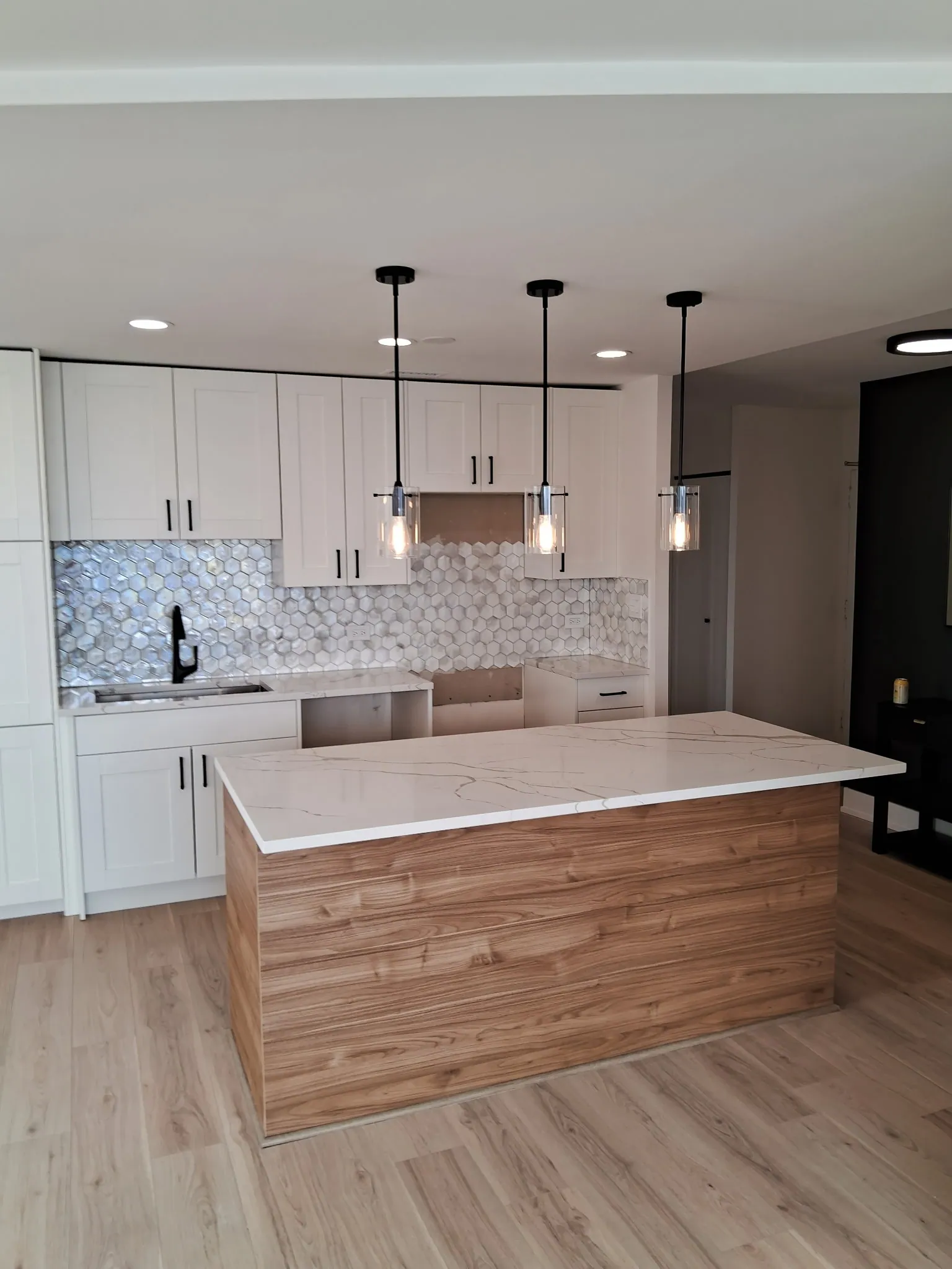 Condo kitchen island with a white veined countertop and wood-grain panel, glass pendants above and new plank flooring