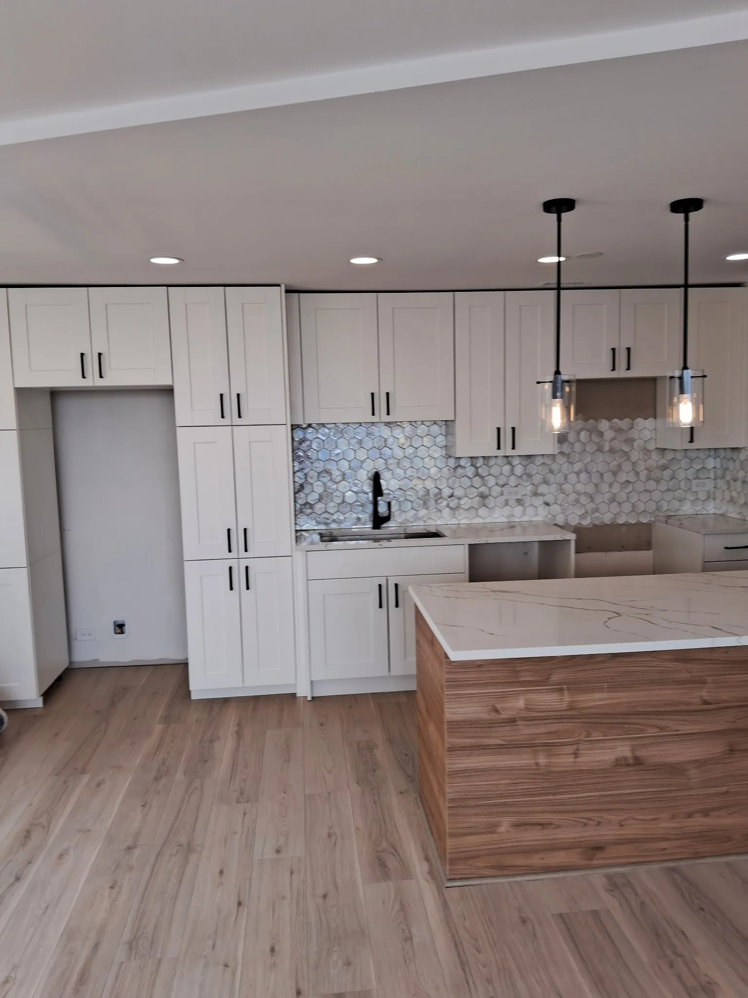 Remodeled condo kitchen in Chicago with white shaker cabinets, a wood-grain island with a white veined countertop and glass pendant lights
