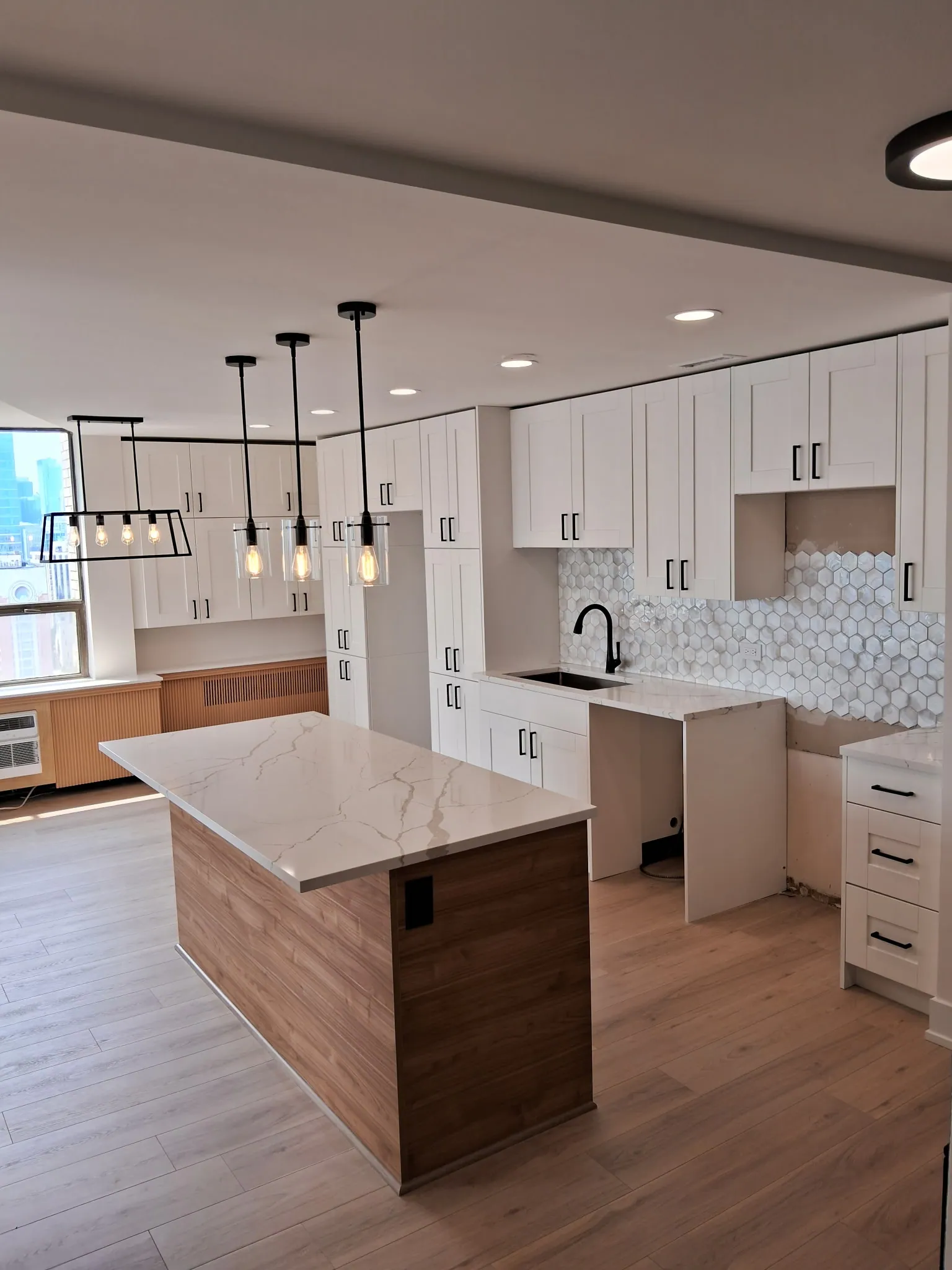Remodeled condo kitchen with white cabinets, black faucet, hexagon tile backsplash and a lantern pendant over the dining area