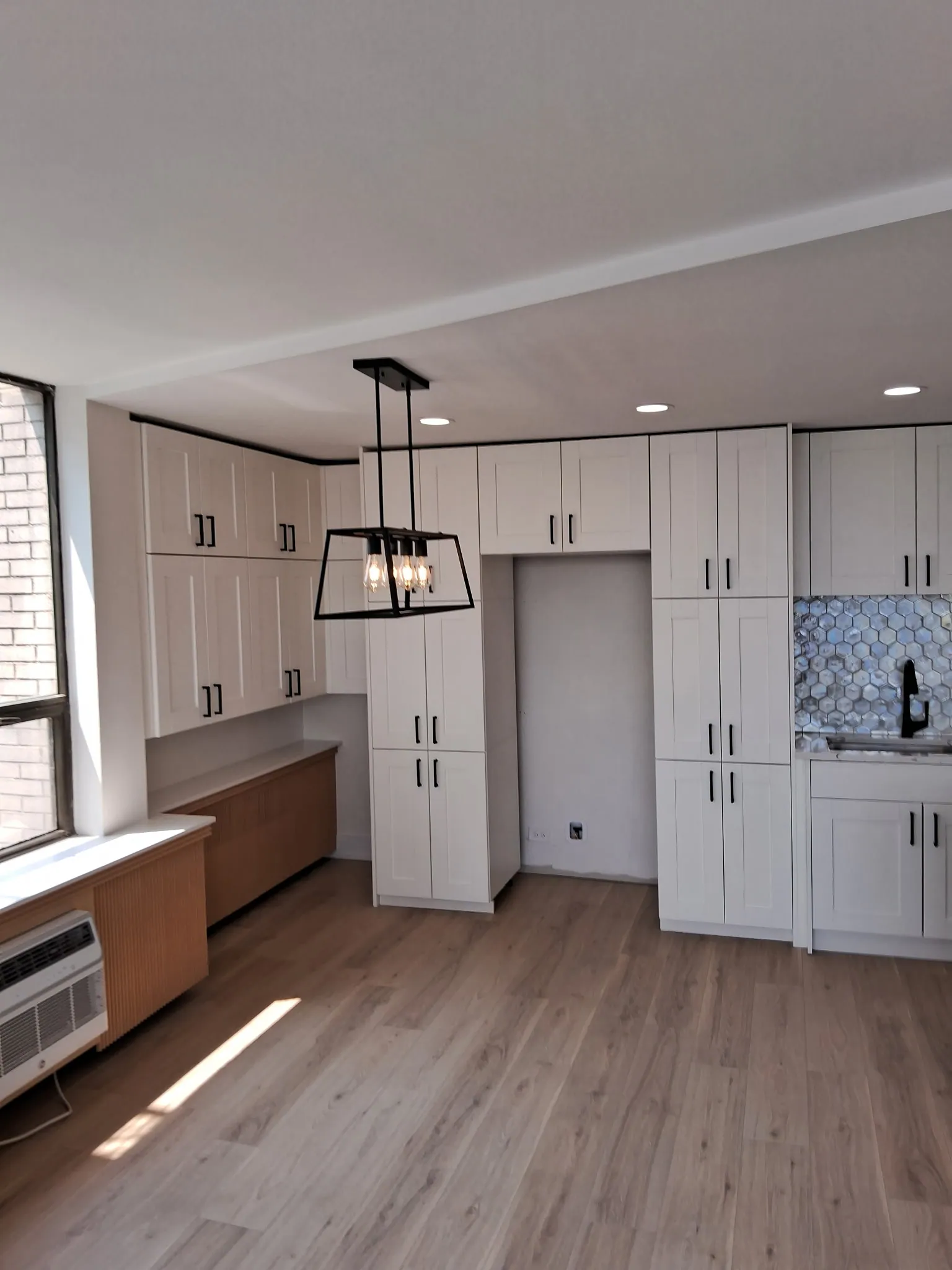 Open-concept condo kitchen and living area with new wood-look plank flooring, white cabinets and a black lantern pendant