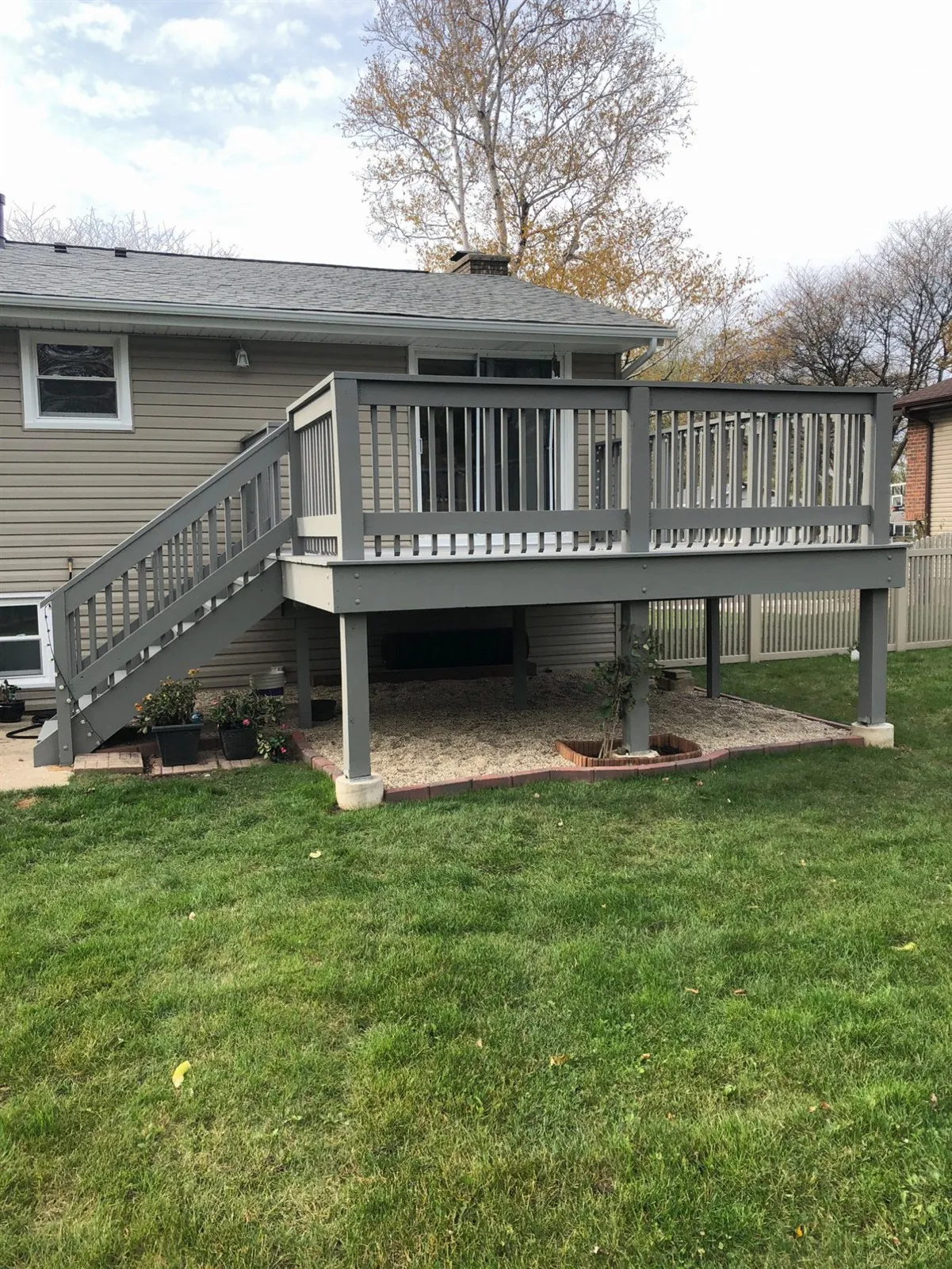 Raised gray deck with railings and stairs, seen from the yard