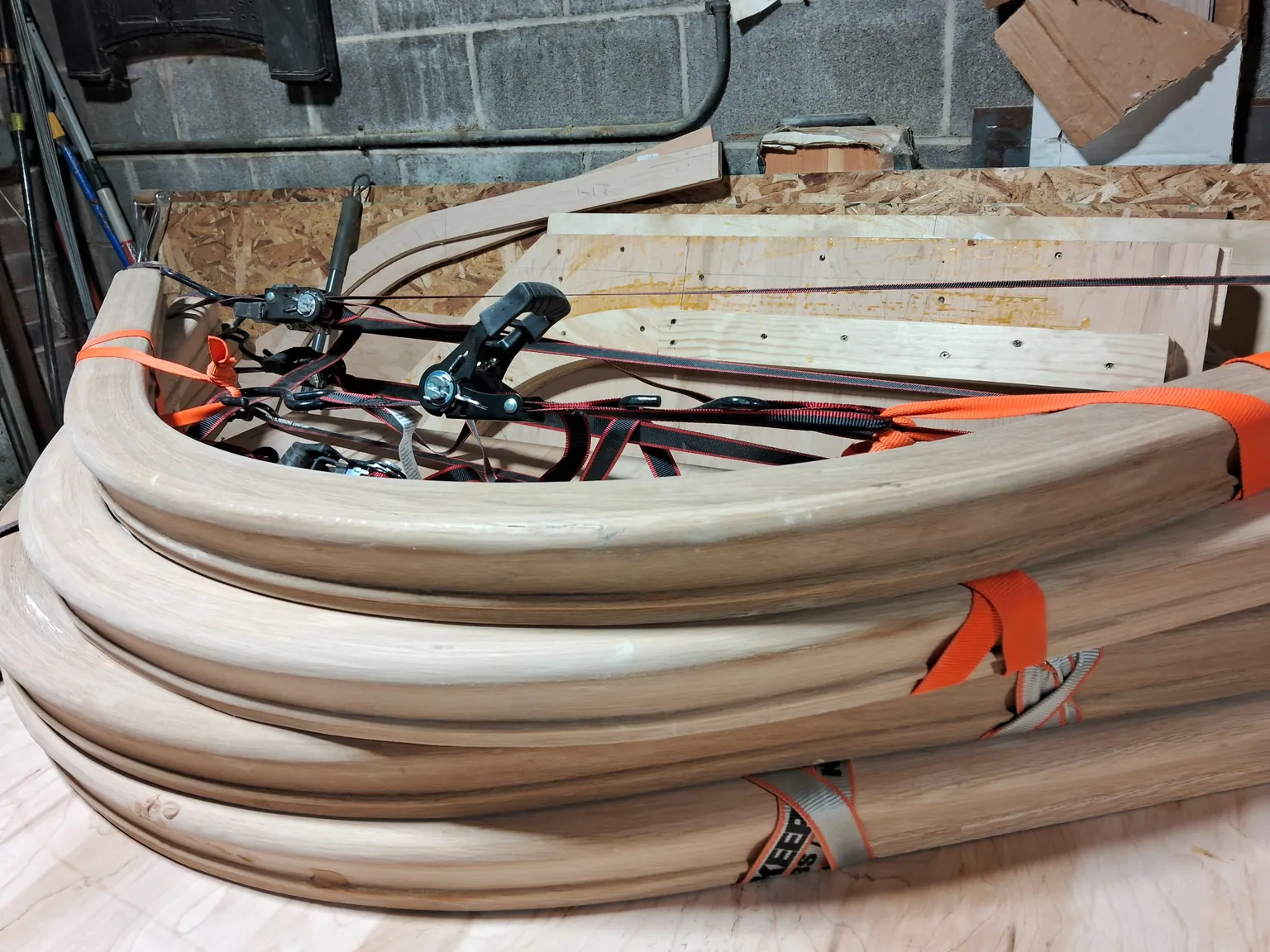Close-up of several curved oak handrail sections stacked on a workbench with orange straps