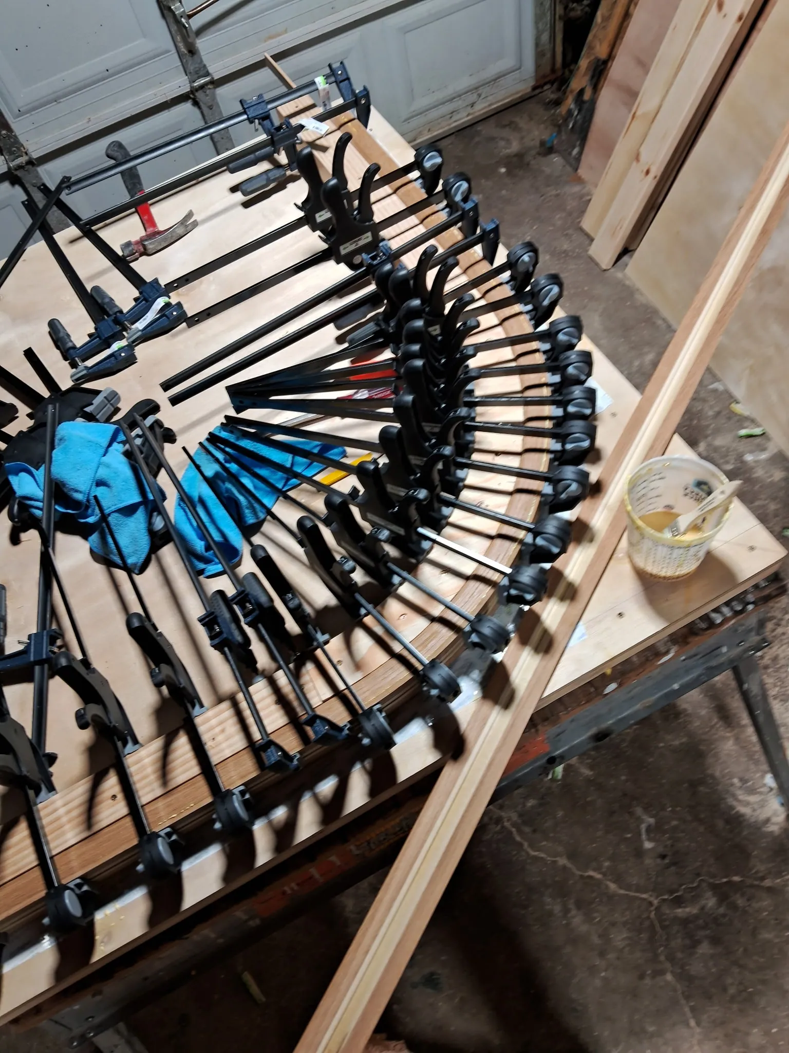 Row of black bar clamps along a curved oak handrail being glued on a plywood form
