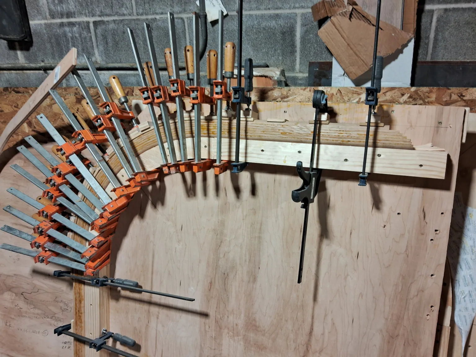 Curved oak handrail strips glued and clamped around a plywood form with orange bar clamps