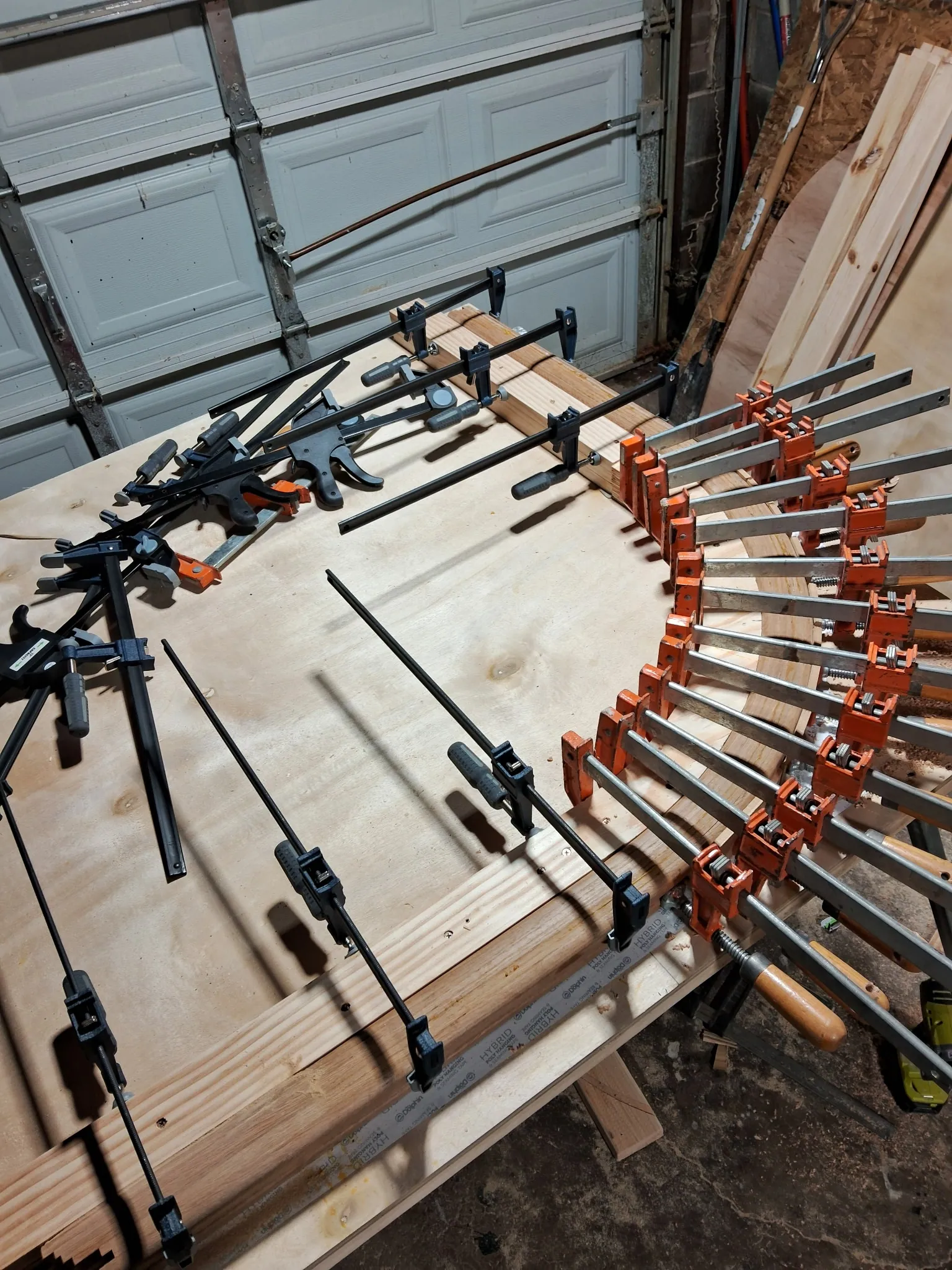 Bent oak handrail glue-up with black and orange bar clamps on a plywood form