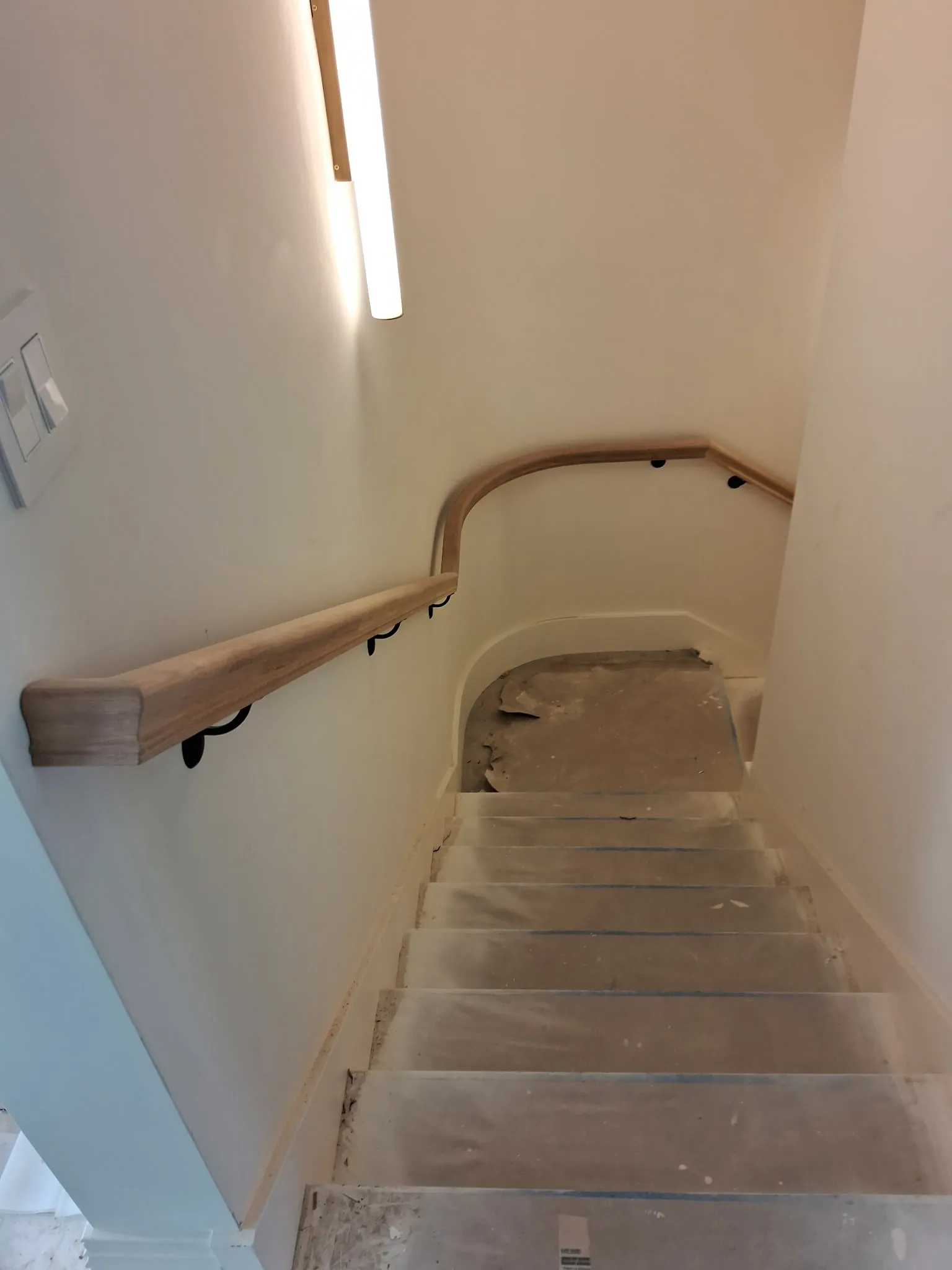 Wall-mounted oak handrail with a return end and black brackets on a stair