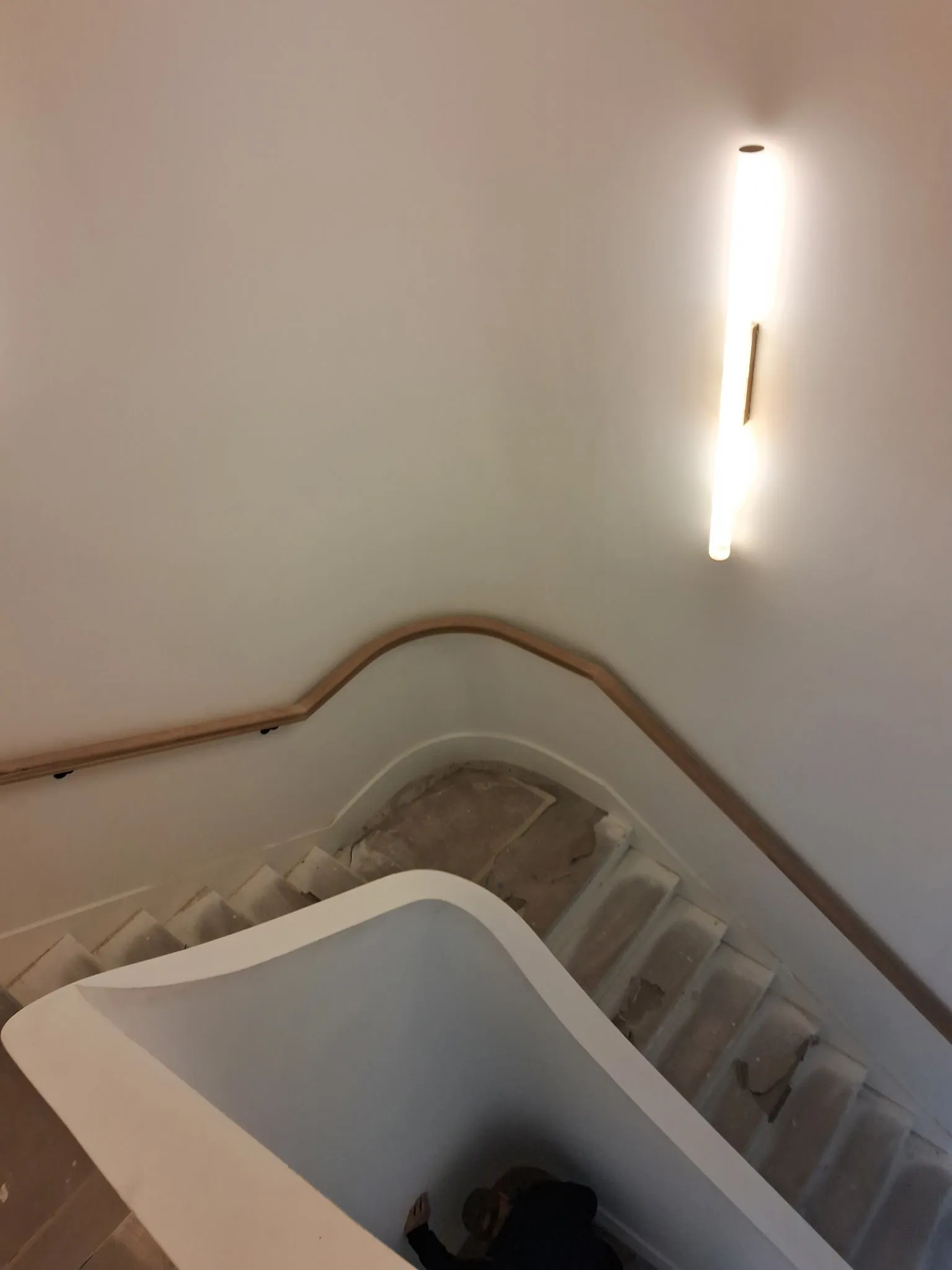 Curved oak handrail at the turn of a stair landing next to a white guard wall