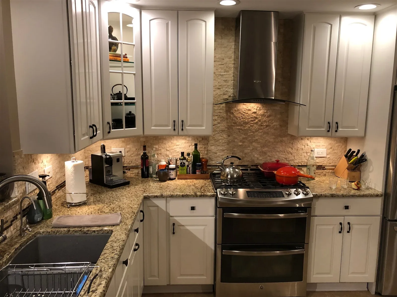 Kitchen with white cabinets, stone backsplash and stainless range hood